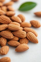 A close-up view of raw almonds scattered on a white surface with a green leaf accent