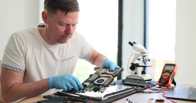 Man technician wearing latex gloves diagnoses computer motherboard in workshop. Professional maintenance service for digital equipment slow motion