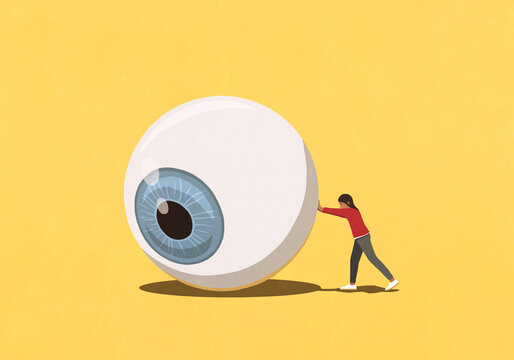 Woman pushing large eyeball on yellow background
