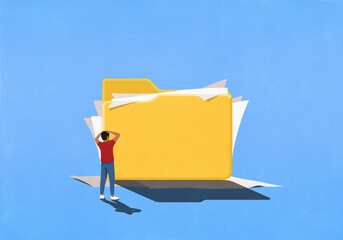 Frustrated man looking at messy paperwork spilling out of large file folder
