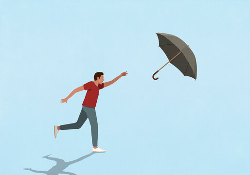 Man chasing umbrella flying in wind against blue background
