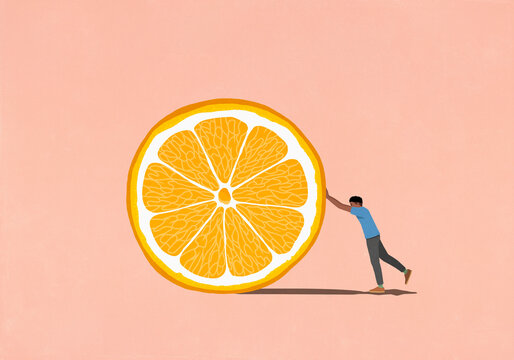 Man pushing large orange slice on pink background
