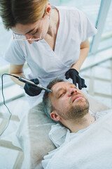 Fototapeta premium A beautician makes a mask on a man's face in a spa salon. Side view of male face during procedure. Pimples and acne on the skin. Injection for a man's face