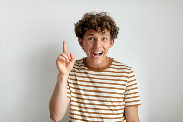 A cheerful young man with curly hair smiles widely while raising his finger, seemingly having an...