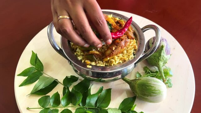 A bowl of vangi bath with brinjal and topped with red chilli and corriander