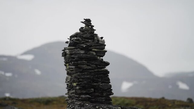 A dark stone cairn in the bleak northern landscape. Misty snow-covered mountains in the background. Parallax shot.