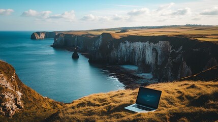 A laptop rests on grassy cliffs overlooking a serene ocean, showcasing a blend of technology and natural beauty.