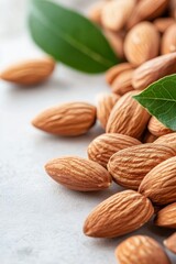 A close-up view of raw almonds scattered on a white surface with a green leaf accent