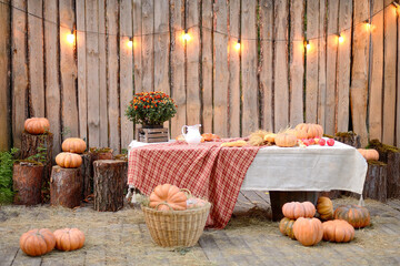 Autumn harvest setting with pumpkins, table, flowers, wooden logs, and fairy lights outdoors