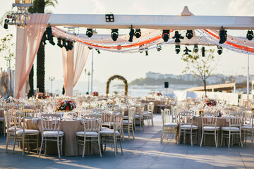 Elegant Outdoor Wedding Reception with Draped Canopy, Floral Centerpieces, and White Chairs...