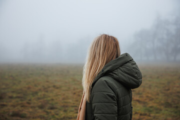 Pensive woman with hooded coat standing in fog alone. Sadness and loneliness concept