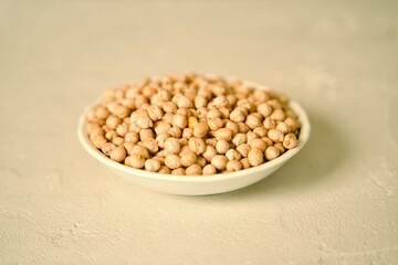 A ceramic plate filled with raw chickpeas placed on a light surface.