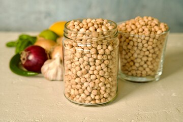 A glass jar filled with raw chickpeas placed on a light surface.