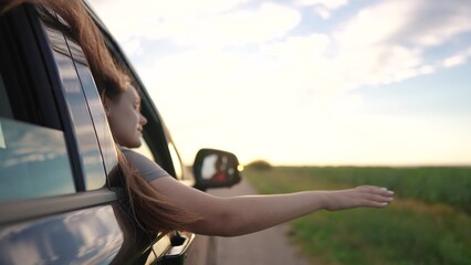 Travel. Girl hand from the car goes backdrop of the sunset. Roadtrip open free concept. Girl in car...