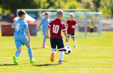 Obraz premium Kids Kicking Football Ball. Boys Play Soccer on Grass Field. Spectators Parents in the Background. Youth Players kicking Soccer Match on grass Stadium. Youth Football Tournament