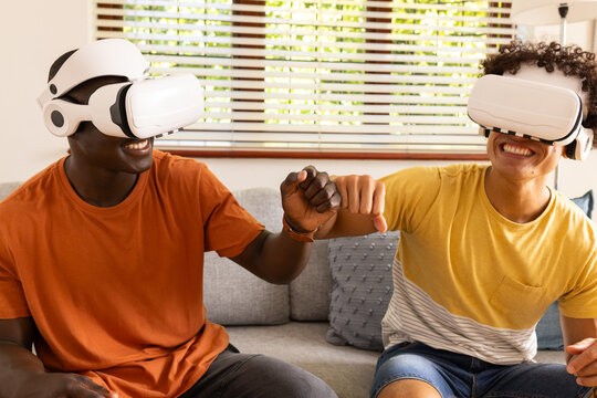 At home, Wearing VR headsets, two diverse male friends fist bumping while enjoying virtual reality g