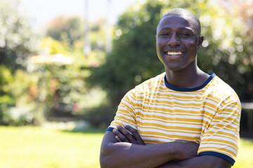 Smiling african american man in striped shirt standing outdoors with arms crossed, enjoying day, cop