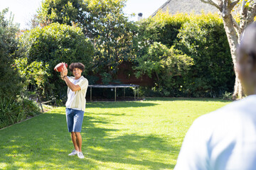 Outdoors, Playing catch, young man throwing football to friend in backyard