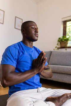 Meditating on yoga mat, african american man in blue shirt practicing mindfulness at home