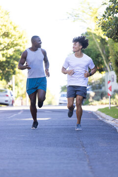 Running together on street, two diverse male friends enjoying outdoor workout and bonding