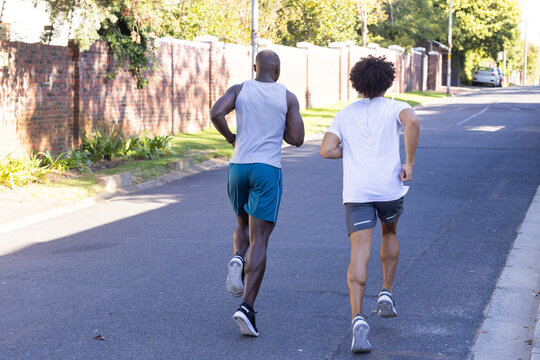 Running outdoors, two diverse male friends exercising together on suburban street in morning