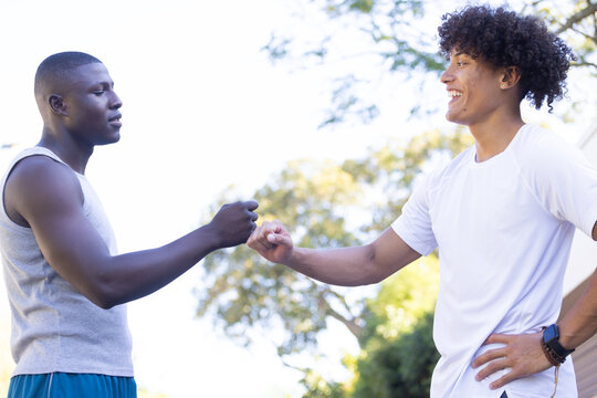 Giving fist bump, two diverse male friends outdoors enjoying time together