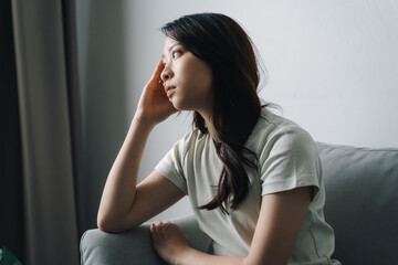 Unhappy lonely depressed woman is sitting on the couch and holding her head.