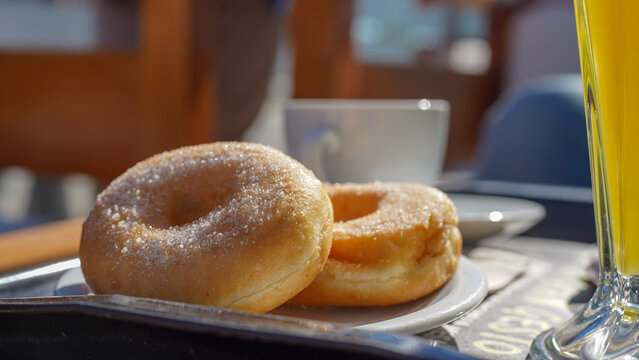 Dos donas glaseadas, reci&eacute;n hechas, descansan en un plato blanco junto a un vaso de jugo de naranja. Un desayuno dulce y tentador, perfecto para cualquier ocasi&oacute;n
