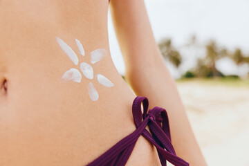 Woman in purple bikini with flower on stomach applying sun tan lotion on back