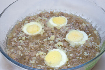 aspic jelly with boiled meat pieces and halved eggs. in glass round saucepan. closeup