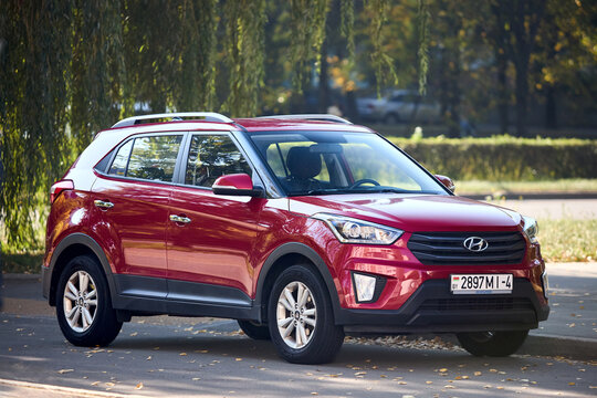 Minsk, Belarus - September, 18 2024: Hyundai Creta Premium 1st generation pre-facelift SUV 2014 2021 red metallic front three quarter view parked in simmer street with foliage background.