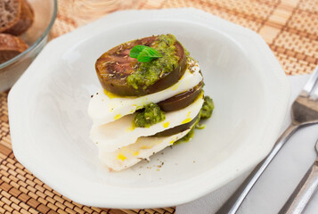 Caprese salad with mozzarella, black tomatoes and pesto in white plate