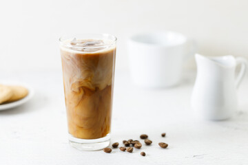 Ice coffee in a tall glass with milk on white marble table.