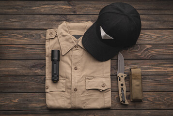 Tactical gear including shirt, cap, knife, and flashlight on wooden surface