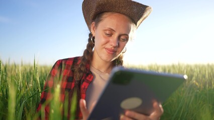 Fototapeta premium Agriculture. A girl eats wheat on a tablet. Agriculture farm technology concept. Farmer lifestyle studying wheat in a. field. Young girl studying on a tablet in a field of wheat.