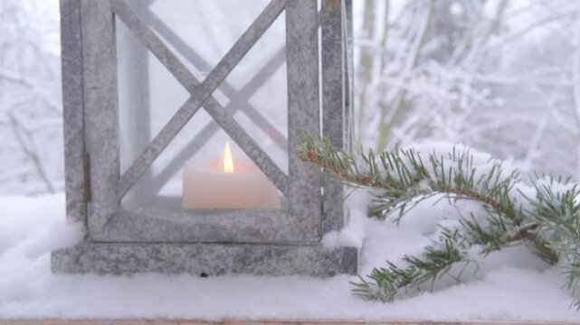Christmas tree decoration, soft flame first Advent candle flickers inside garden lantern with snow gently falling in background for wintery feel, cozy Christmas scene