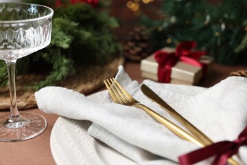 Christmas place setting with plate, napkin, glass and cutlery on brown table, closeup