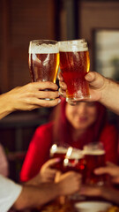 Close-up of fans clinking glasses, beer foaming at top. Behind, blurred group adds energy to festive scene. Selective focus. Concept of Oktoberfest, brewery, vacation, Friday mood.