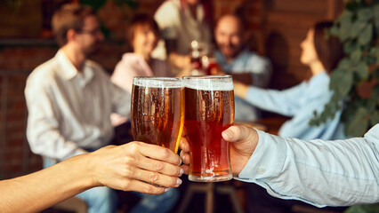 Close-up cheers, while blur of friends behind celebrate with raised glasses. Scene set for a great game day with friends and beer. Concept of Oktoberfest, brewery, vacation, Friday mood.