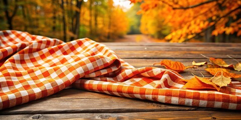 Vibrant orange and white checked fabric drapes elegantly over a rustic wooden table, evoking a warm and cozy atmosphere perfect for autumnal or country-themed designs.