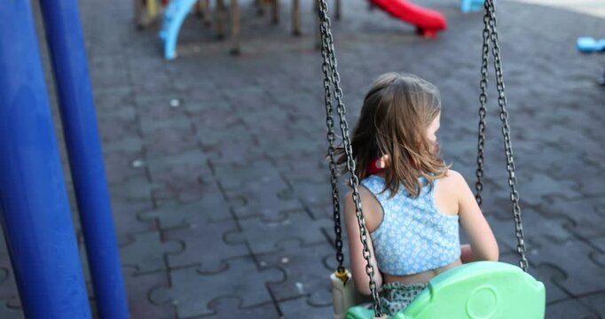 Little girl rides on swing against children slide on modern playground at daytime. Concept of entertainment and recreation in childhood slow motion