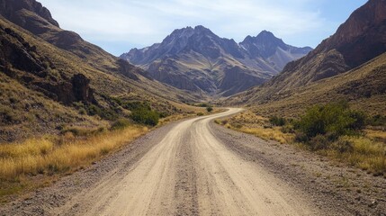 Fototapeta premium A rural dirt road cutting through a rugged mountain landscape, with dramatic peaks and a clear, open sky.