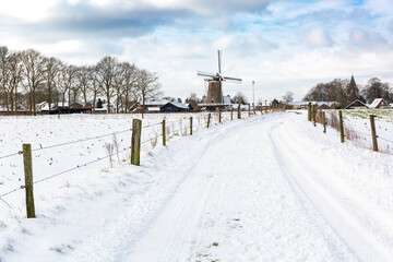 Dutch winter landscape with snowy road and windmill in the background, Garderen, The Netherlands
