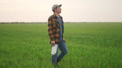 farmer with tablet in the field. lifestyle business finance nature and people concept. a farmer in a hat and plaid shirt walks through a green field with a tablet in his hands