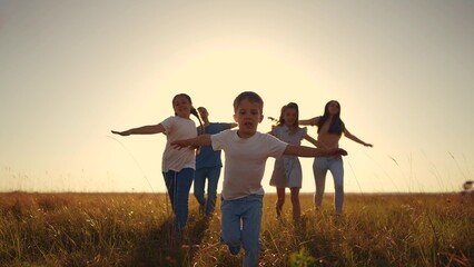 Fototapeta premium children run across the field. people and family concept. a group of happy children running across a large field with their arms outstretched, sunset in the background lifestyle