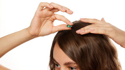Fototapeta premium Hands applying small capsule treatment to scalp, representing hair care and beauty wellness routine against white studio background. Concept of beauty, fashion, appearance, self care. Ad