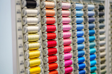 Fototapeta premium Close-up of colored sewing threads of different colors on display in a sewing shop. It is multicolored and made of textile sewing threads.