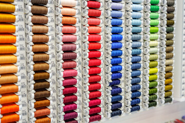 Close-up of colored sewing threads of different colors on display in a sewing shop. It is multicolored and made of textile sewing threads.