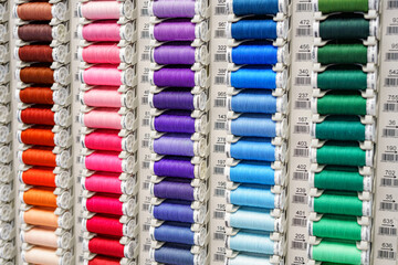Close-up of colored sewing threads of different colors on display in a sewing shop. It is...