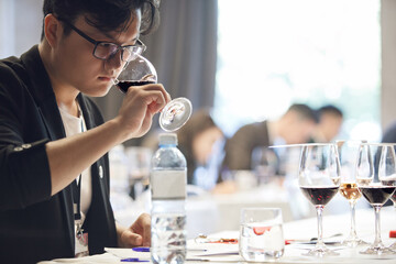 Focused Asian Sommelier Evaluates Aroma of Red Wine During Blind Tasting Event.